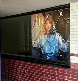 Photo of blonde woman in satin jacket hangs on white and red brick exterior