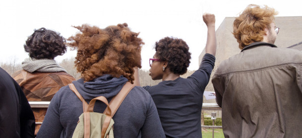 Students gather on campus; one raises fist