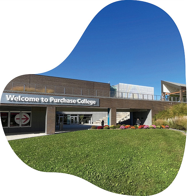 Entrance to Purchase College with 'Welcome to Purchase College' sign, brick buildings, green lawn, and colorful flowers under a blue sky.