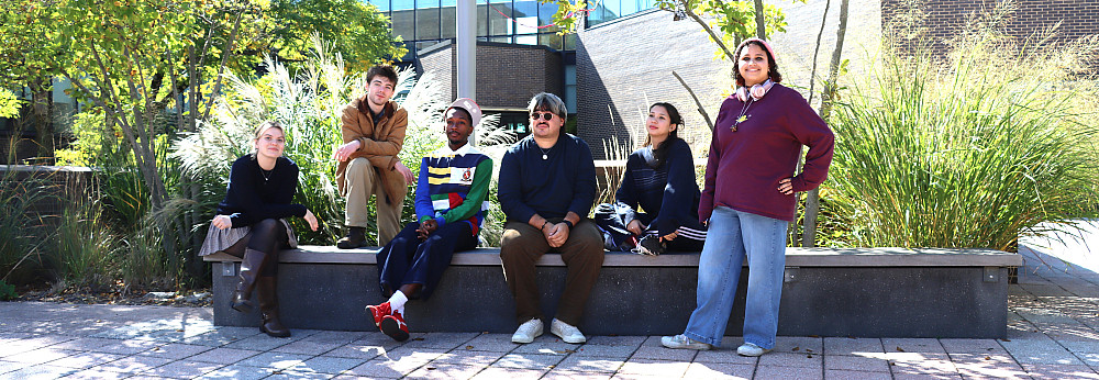 Students gather on a bench outdoors on campus.