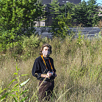 Student with camera stands in a green space.