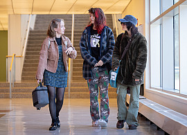 Three students talking and walking in the Humanities lobby