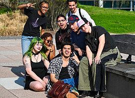 group of students sitting and standing with grass and brick building behind