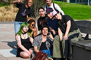 group of students sitting and standing with grass and brick building behind