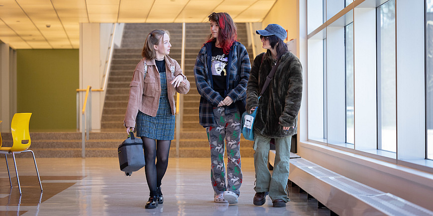 Three students talking and walking in the Humanities lobby