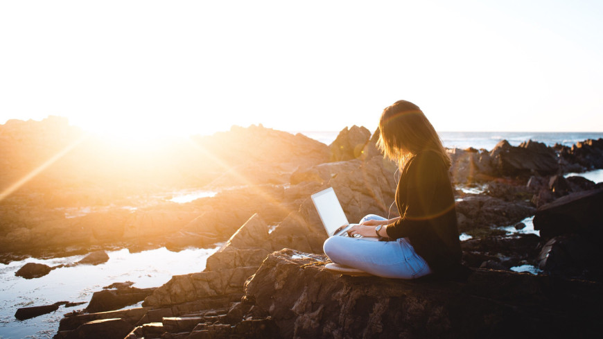 Study anywhere (student uses laptop on a on a rock near the shore)