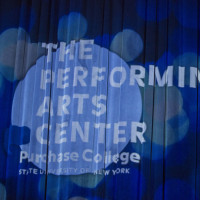The PAC logo projected on the PepsiCo Theatre's stage curtain.