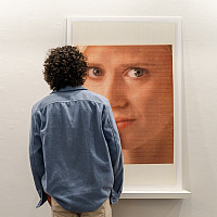 A gallery visitor wearing a blue shirt seen from behind looking at art on the wall.