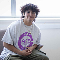 Two students wearing white t-shirts with purple ACE logo sit in chairs, smiling.