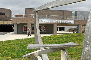 Person walks in distance with Welcome to Purchase College sign on brick building