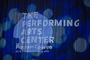 The PAC logo projected on the PepsiCo Theatre's stage curtain.