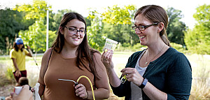 Student and professor outdoors looking at a small container.