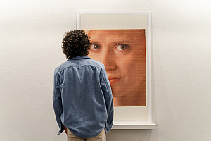 A gallery visitor wearing a blue shirt seen from behind looking at art on the wall.