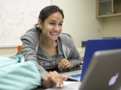 Student smiles looking at a laptop.