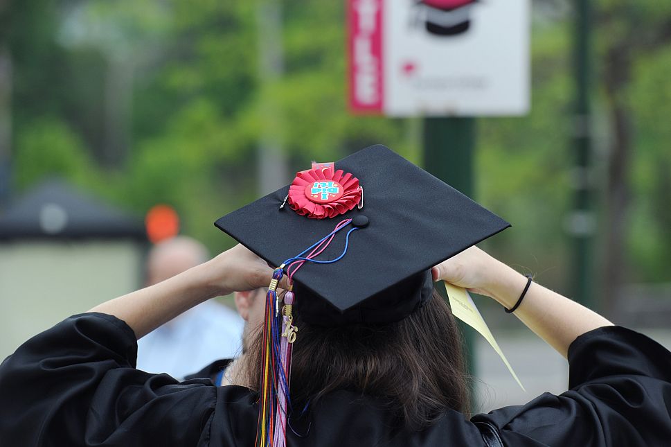 Graduate from behind adjusts commencement cap with flower.