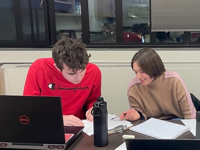 Boy in red shirt and girl in beige shirt studying together at a table.