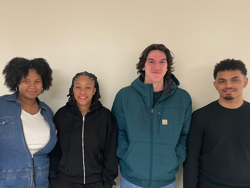 Four S-STEM students are standing against a beige wall and smiling.