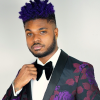 Black man in purple tux with one hand on his bowtie