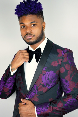 Black man in purple tux with one hand on his bowtie