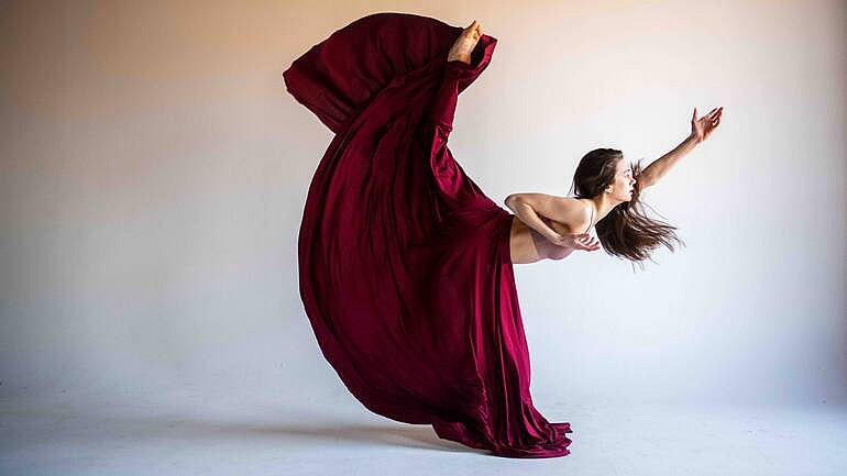 Dancer in long dark red skirt with leg extended up