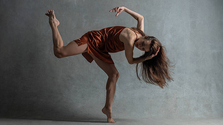 Dancer in burgundy striking a pose bent over on one foot