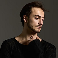 Portrait of Denis Erkan Sancak on brown background looking down to the right