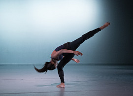 Dancer in motion, bending over right leg while left leg extended behind and above.