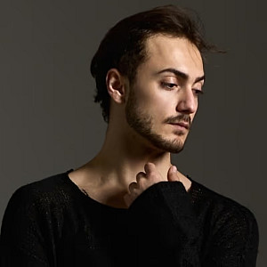 Portrait of Denis Erkan Sancak on brown background looking down to the right