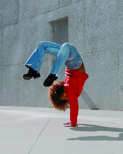 Dava Huesca in jeans and red hoodie doing a handstand on the sidewalk with knees bent