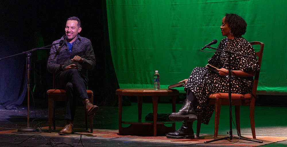 Justin Torres and Angela Flournoy sit on chairs on stage with a green backdrop.