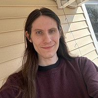 Student Maxim Olsen with a slight smile outside in front of house siding.