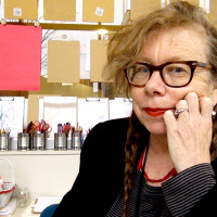 face of woman with glasses, red lipstick and two long braids in front of art supplies