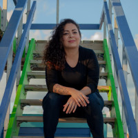 author Jaqira Diaz sitting on the steps of a lifeguard house on the beach