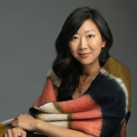 Poet Monica Youn sitting in a chair with a shawl over her shoulders.