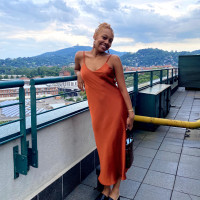 Student Marirosa Crawford in and Orange Slip dress standing next to a railing with a mountainside view in the background.