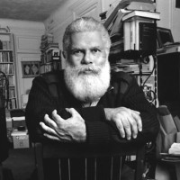 Author Samuel R. Delany sitting in a chair with a background of books