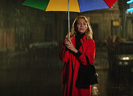 Woman in a red coat in the rain holding a rainbow colored umbrella