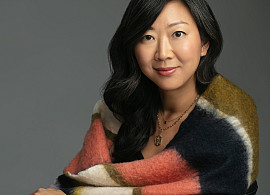 Poet Monica Youn sitting in a chair with a shawl over her shoulders.