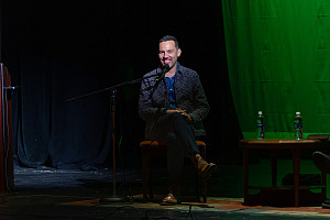 Justin Torres sits on stage with dark background smiling
