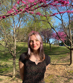 Student Lilliam Cheever smiling with her arms crossed behind her in from of a blooming tree with pink flowers