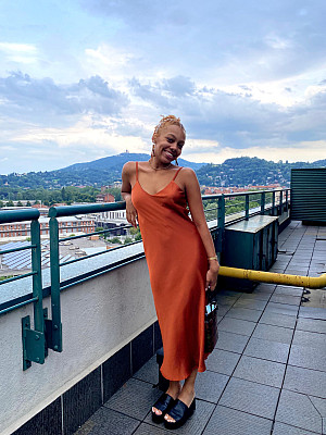 Student Marirosa Crawford in and Orange Slip dress standing next to a railing with a mountainside view in the background.