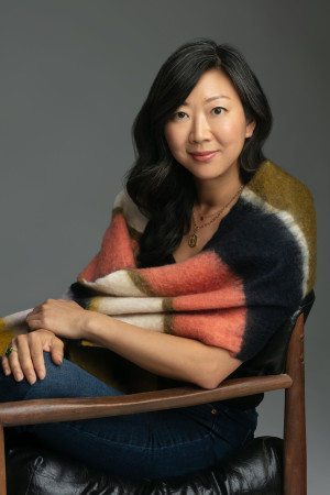 Poet Monica Youn sitting in a chair with a shawl over her shoulders.