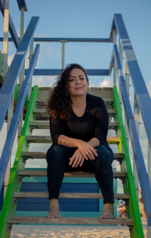 author Jaqira Diaz sitting on the steps of a lifeguard house on the beach