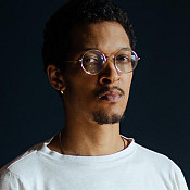 Caleb Eberhardt '12 sits in a chair against dark background.