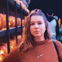 Young woman in orange turtleneck in front of rows of jack-o-lanters