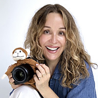 Kate Hart Finnigan in blue shirt, white pants sits holding camera on one knee