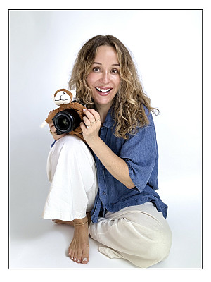 Kate Hart Finnigan in blue shirt, white pants sits holding camera on one knee
