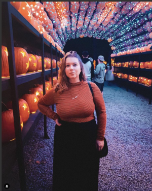 Young woman in orange turtleneck in front of rows of jack-o-lanters