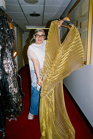 Suzi-Gomez-Pizzo holds up a gold gown costume.