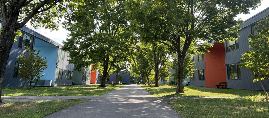 Photograph of the Olde apartments. Several blue buildings surrounded by greenery and two benches.